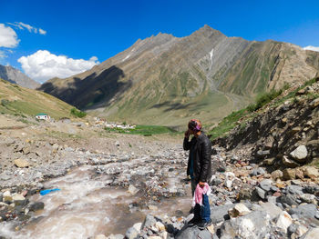 Man standing on rock by stream against mountain