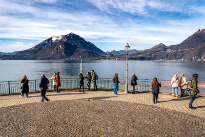 Tourists standing on observation point by lake against mountains during sunny day
