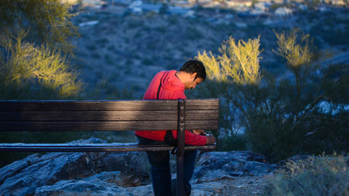 Man sitting on bench against mountains during sunset