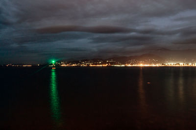 Illuminated cityscape by sea against sky at night