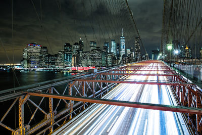 Light trails on road amidst buildings against sky at night