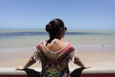 Rear view of woman leaning on railing against beach on sunny day