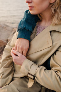 Crop man embracing blond girlfriend in outerwear and looking away while sitting on stony coast of rippling sea on cloudy day in aviles, spain