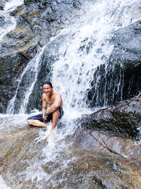 Full length of shirtless man enjoying waterfall