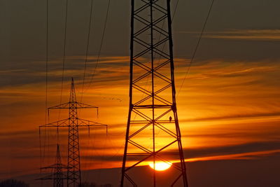 Silhouette electricity pylons against sky during sunset