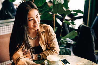 Happy young woman using phone while sitting on table