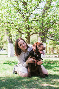 Smiling young caucasian woman is hugging her puppy of chocolate labrador retriever dog. 