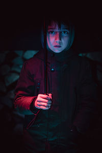 Portrait of young woman standing against black background