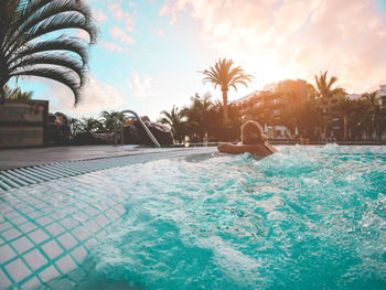 Swimming pool by palm trees against sky