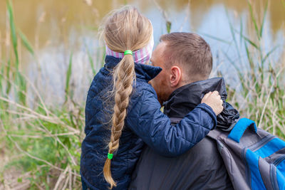 Father and daughter sitting by lake nature lanscape little girl hugging with dad fathers day concept