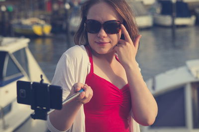 Beautiful woman holding monopod while taking selfie through smart phone at harbor