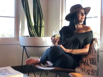 Thoughtful mid adult woman with drink sitting on chair at home