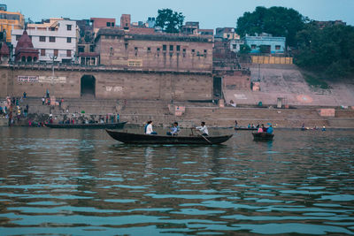 People on boats in river against buildings