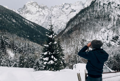 Rear view of young man taking photos of mountains in winter.