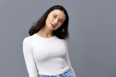 Portrait of young woman standing against gray background