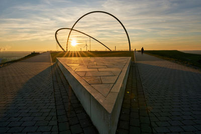 Footpath by street against sky during sunset