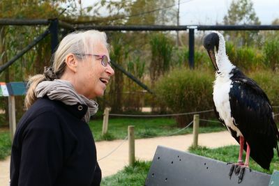 Side view of senior woman standing by bird perching on metal