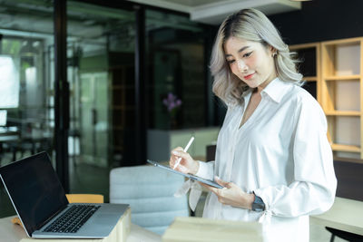 Young woman using mobile phone while standing in cafe