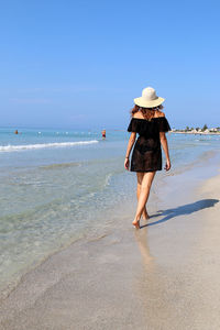 Rear view of woman on beach against sky