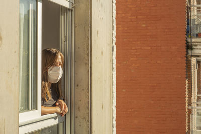 Side view of woman wearing mask looking through window