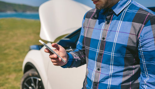 Midsection of man holding mobile phone while standing on land