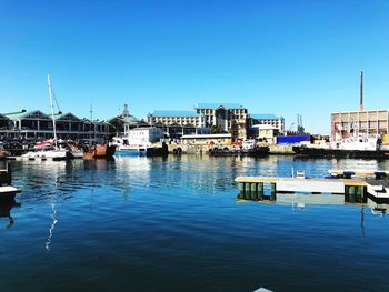 Boats moored at harbor against clear blue sky