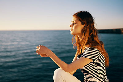 Side view of young woman in sea against sky