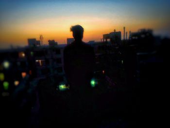 Close-up of silhouette man against illuminated cityscape at sunset