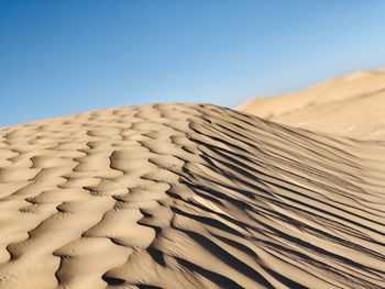 Sand dunes in desert against clear blue sky