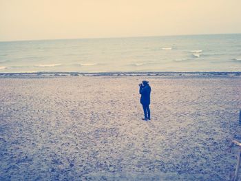 Rear view of man standing on beach against sky during sunset