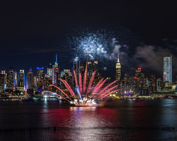 Firework display over river in illuminated city at night