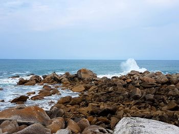 Rocks on shore by sea  with spray against sky