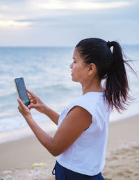 Side view of young woman using mobile phone while standing at beach