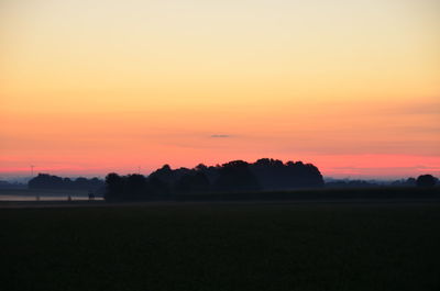 Scenic view of silhouette field against orange sky