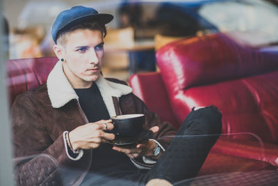 Handsome man sitting with coffee at cafe seen from window