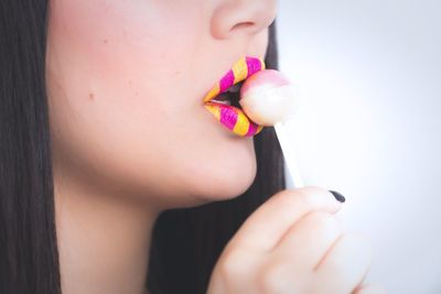 Cropped image of woman with yellow and pink lipstick licking lollipop