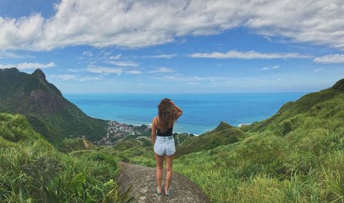 Panoramic view of woman looking out at sea and mountains 