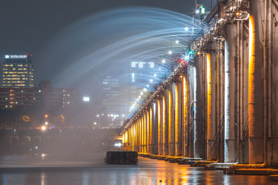 Illuminated bridge over river against sky at night