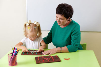 Side view of mother and daughter sitting on table