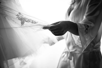 Midsection of woman holding wedding dress at home