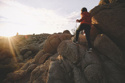 Rear view of boy climbing on rock formations at joshua tree national park during sunset