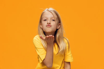 Portrait of girl blowing kiss standing against orange background