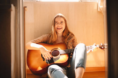 Cheerful young woman holding guitar while sitting on balcony floor