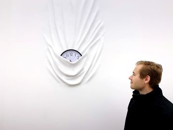 Young man looking at clock in white wall