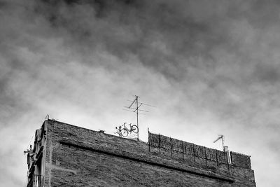 Low angle view of bicycles by television aerial on building terrace against sky