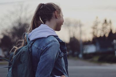 Side view of woman with backpack standing on road during sunset