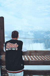 Rear view of man standing by railing against sky