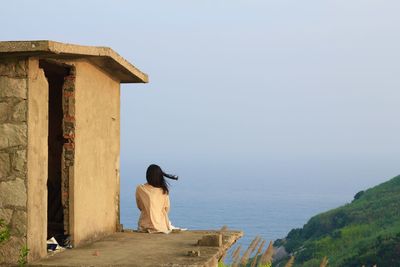 Rear view of woman sitting on rooftop and looking at view