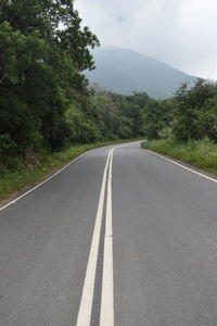 Empty road amidst trees against sky