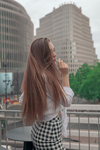 Side view of young woman standing outdoors against sky